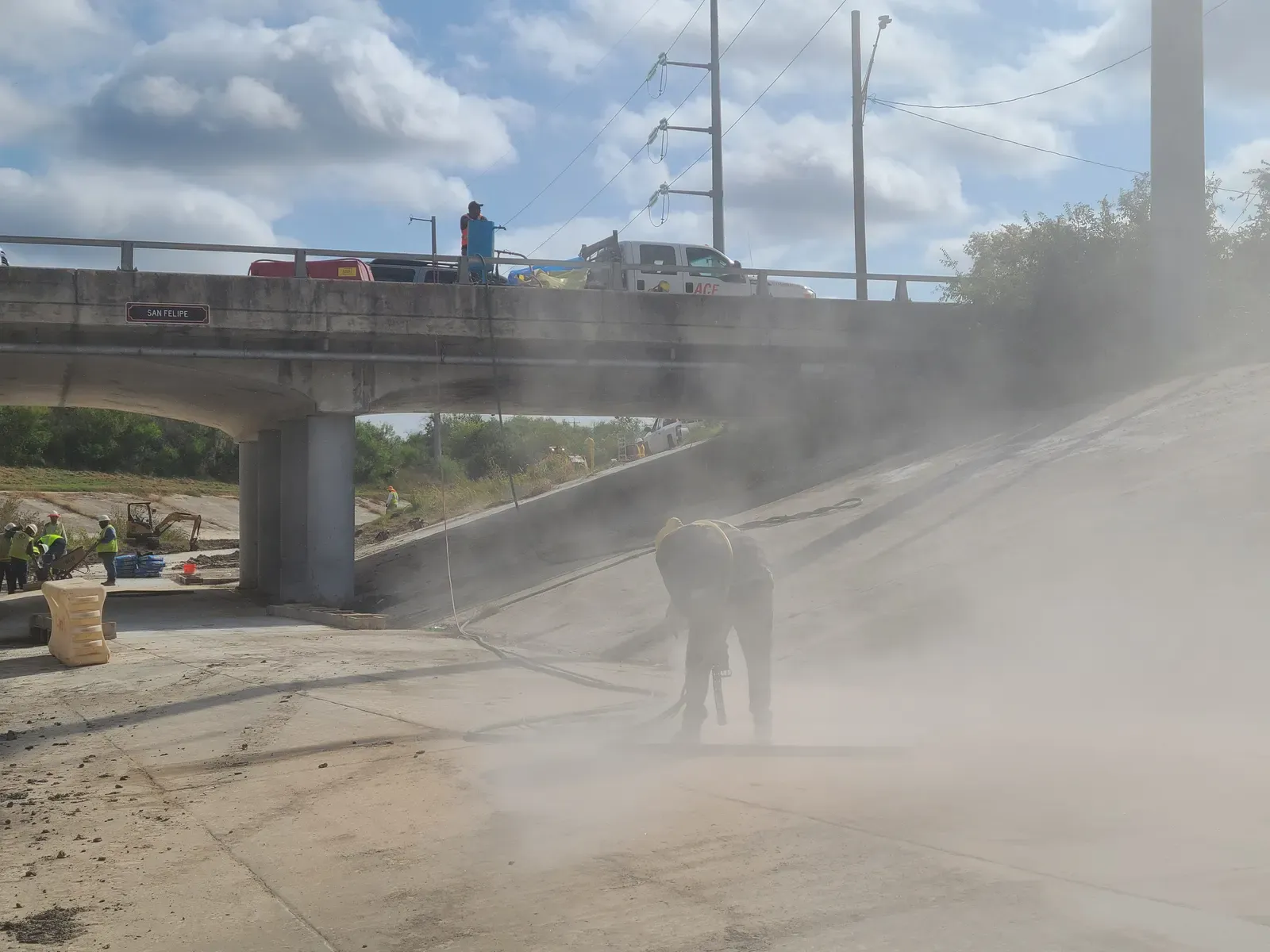 Worker sandblasting a concrete slope beneath a highway bridge