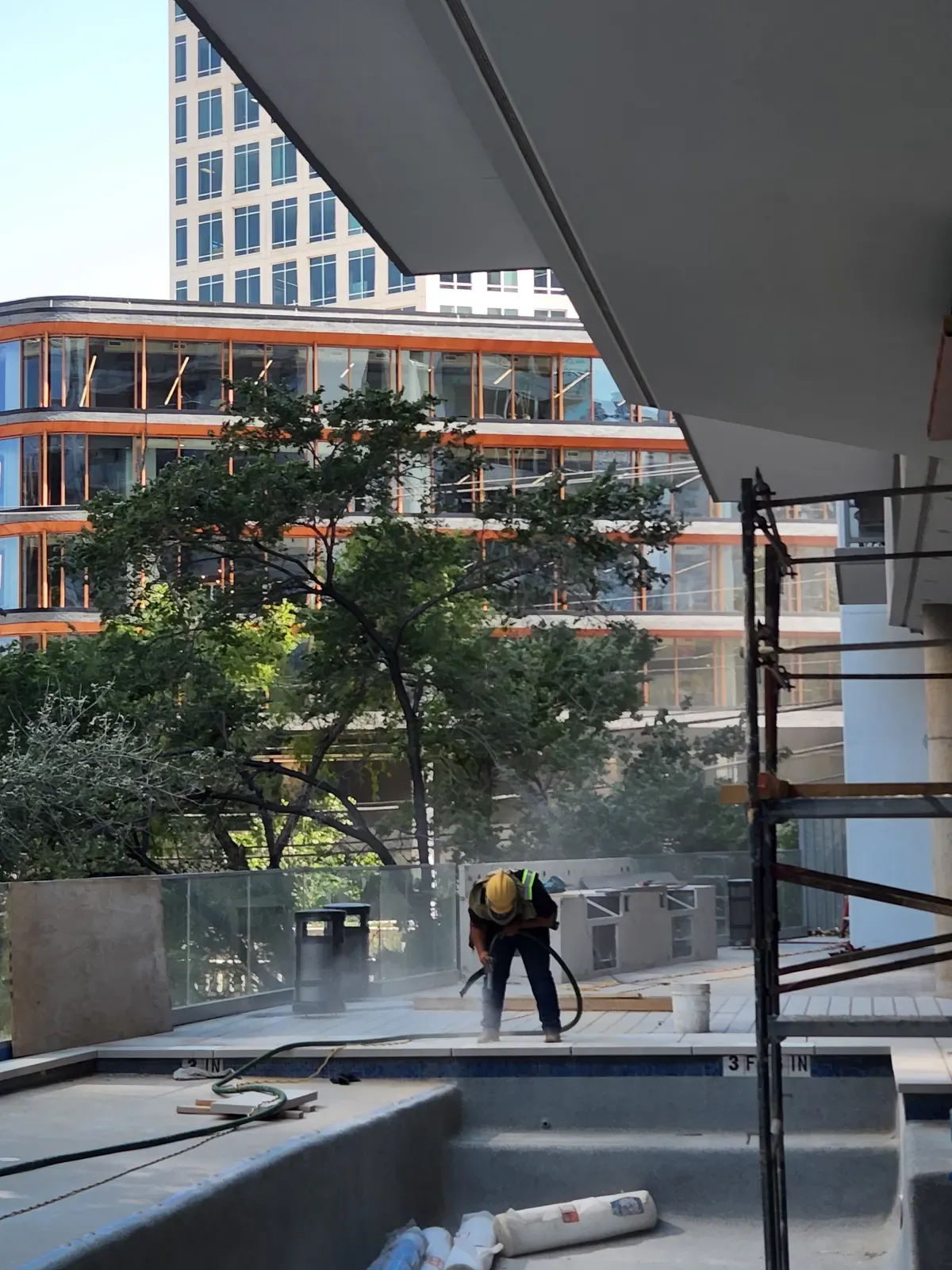Technician sandblasting a rooftop pool deck among high-rise buildings