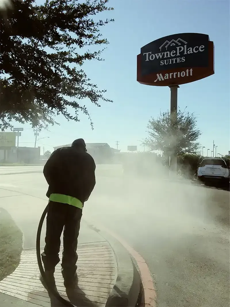 Technician sandblasting concrete beside a TownePlace Suites hotel sign
