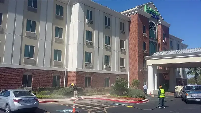 Worker in hi-vis gear sandblasting pavement in a hotel parking lot