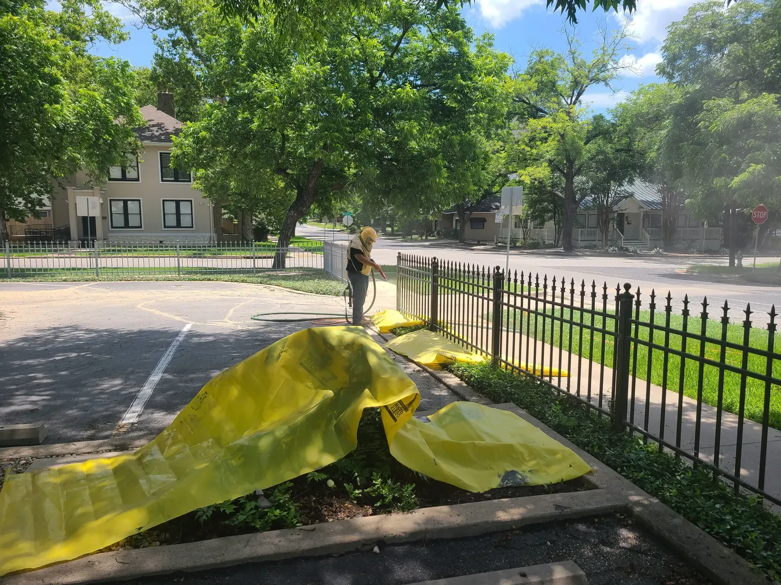 Yellow tarp protecting landscaping while an iron fence is blasted
