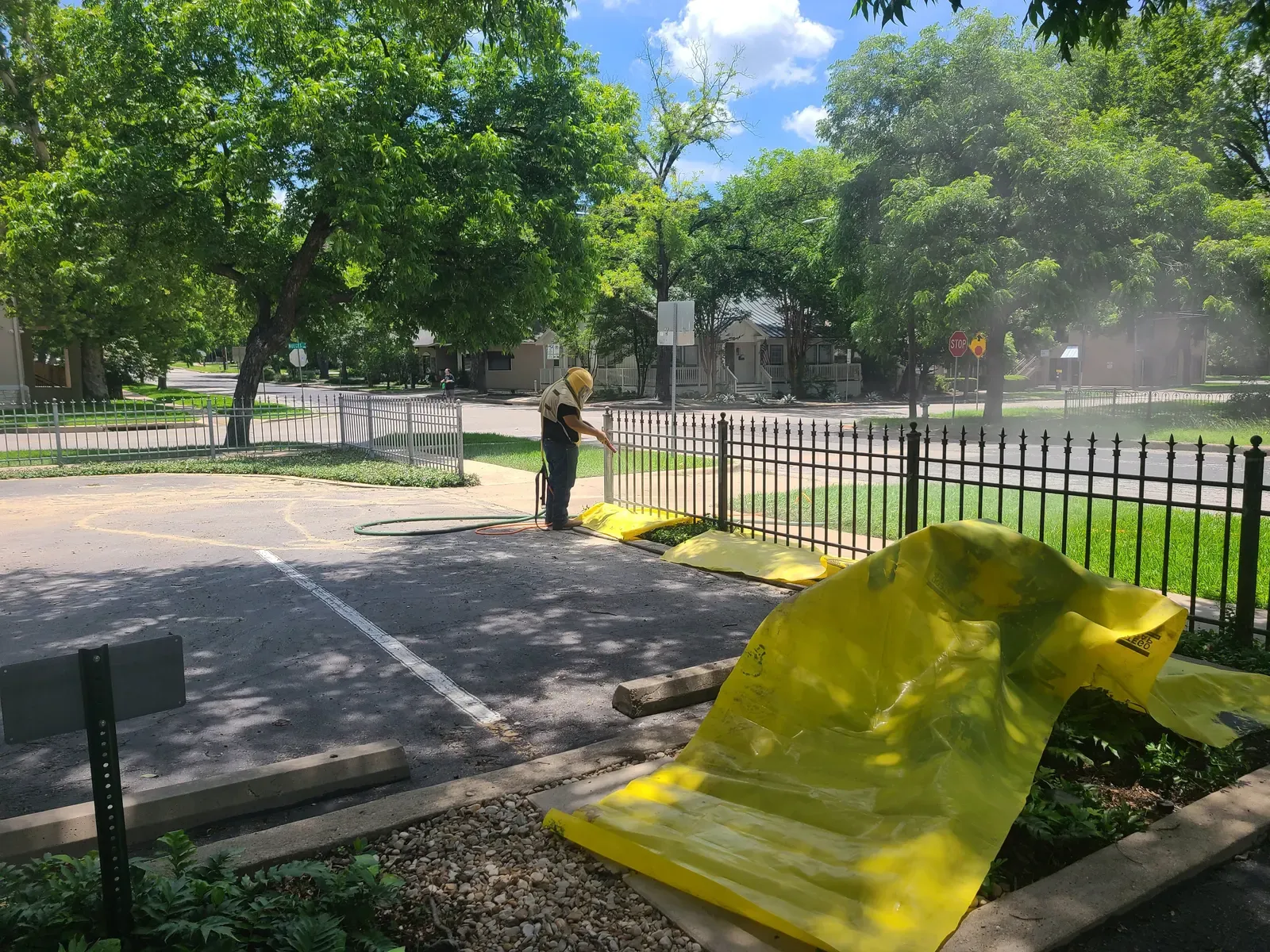Technician sandblasting a parking lot iron fence over a yellow tarp