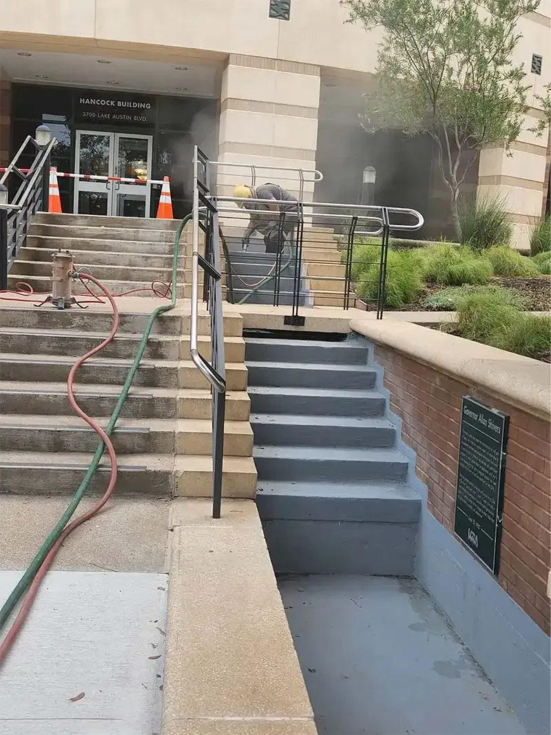Crew sandblasting concrete entry stairs at an office building
