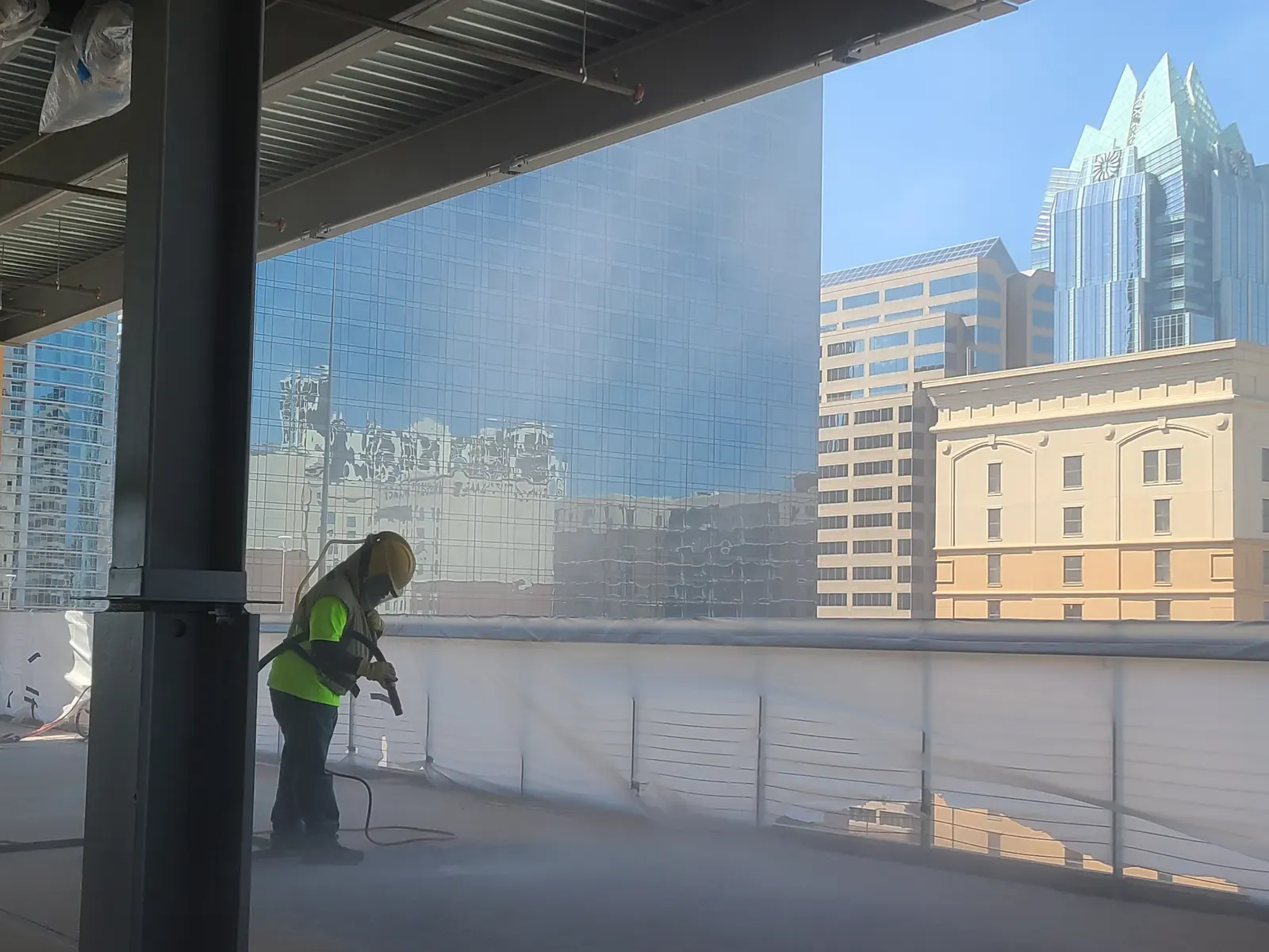 Technician sandblasting a parking garage deck overlooking downtown Austin