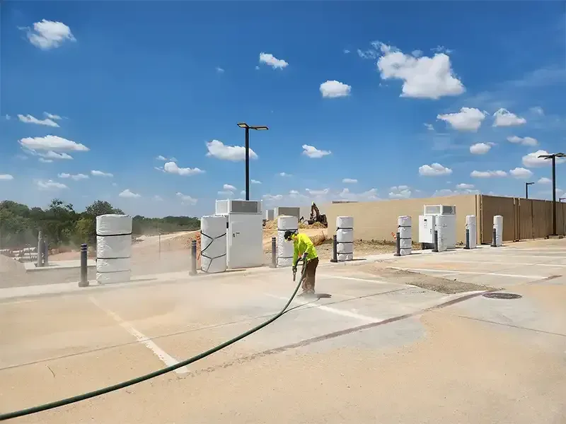 Crew member sandblasting a concrete lot under a blue Texas sky