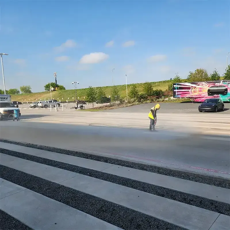 Worker blasting old markings off a large parking lot