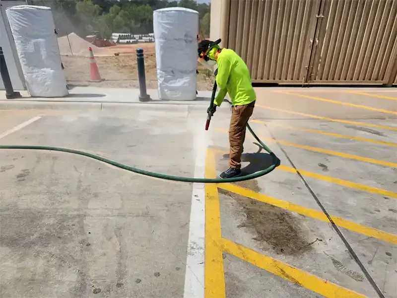 Technician blasting yellow striping off a parking lot crosswalk