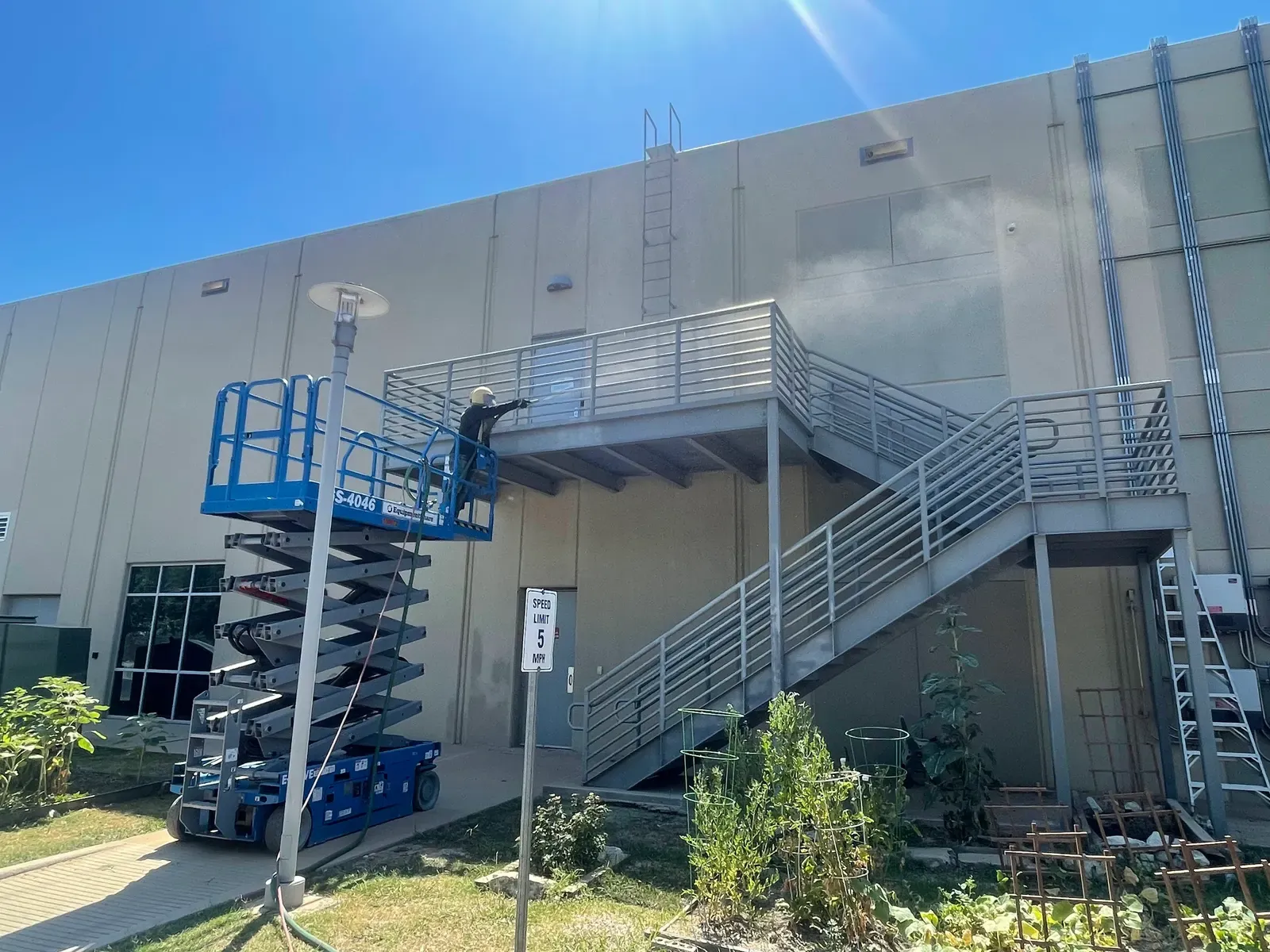 Scissor lift crew sandblasting a warehouse exterior wall and stairway