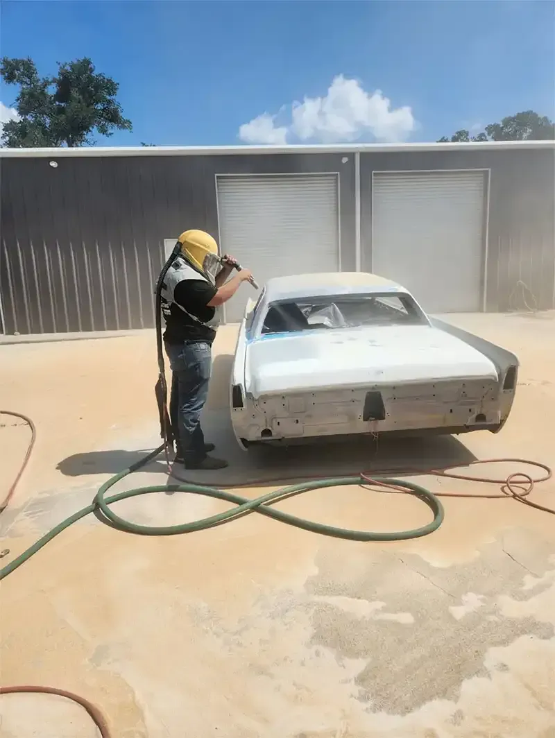 Technician sandblasting a classic sedan outside a shop