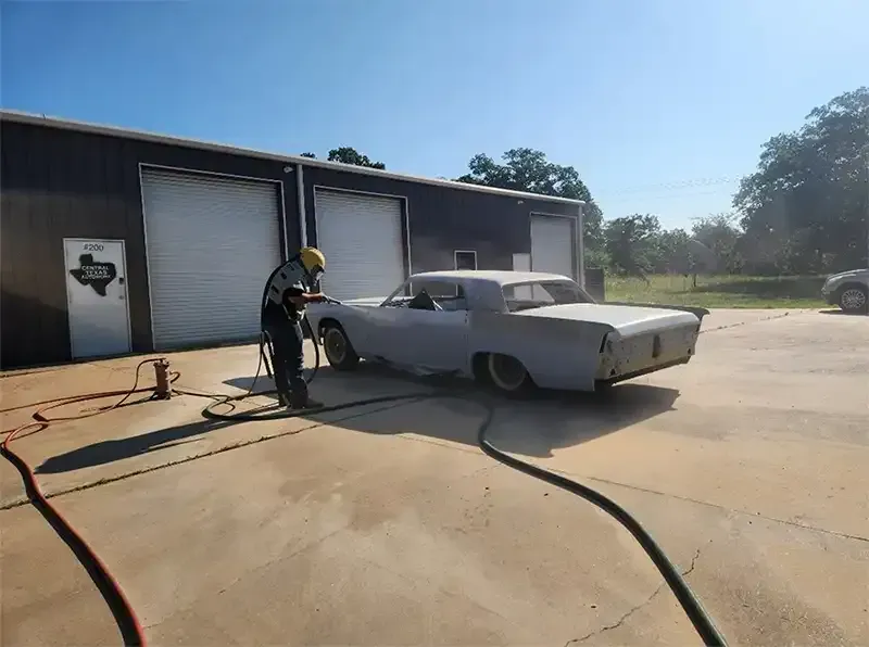 Classic sedan being blasted outside a metal shop building