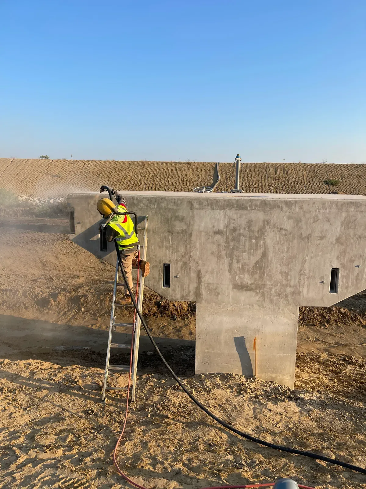 Technician on a ladder sandblasting a concrete structure
