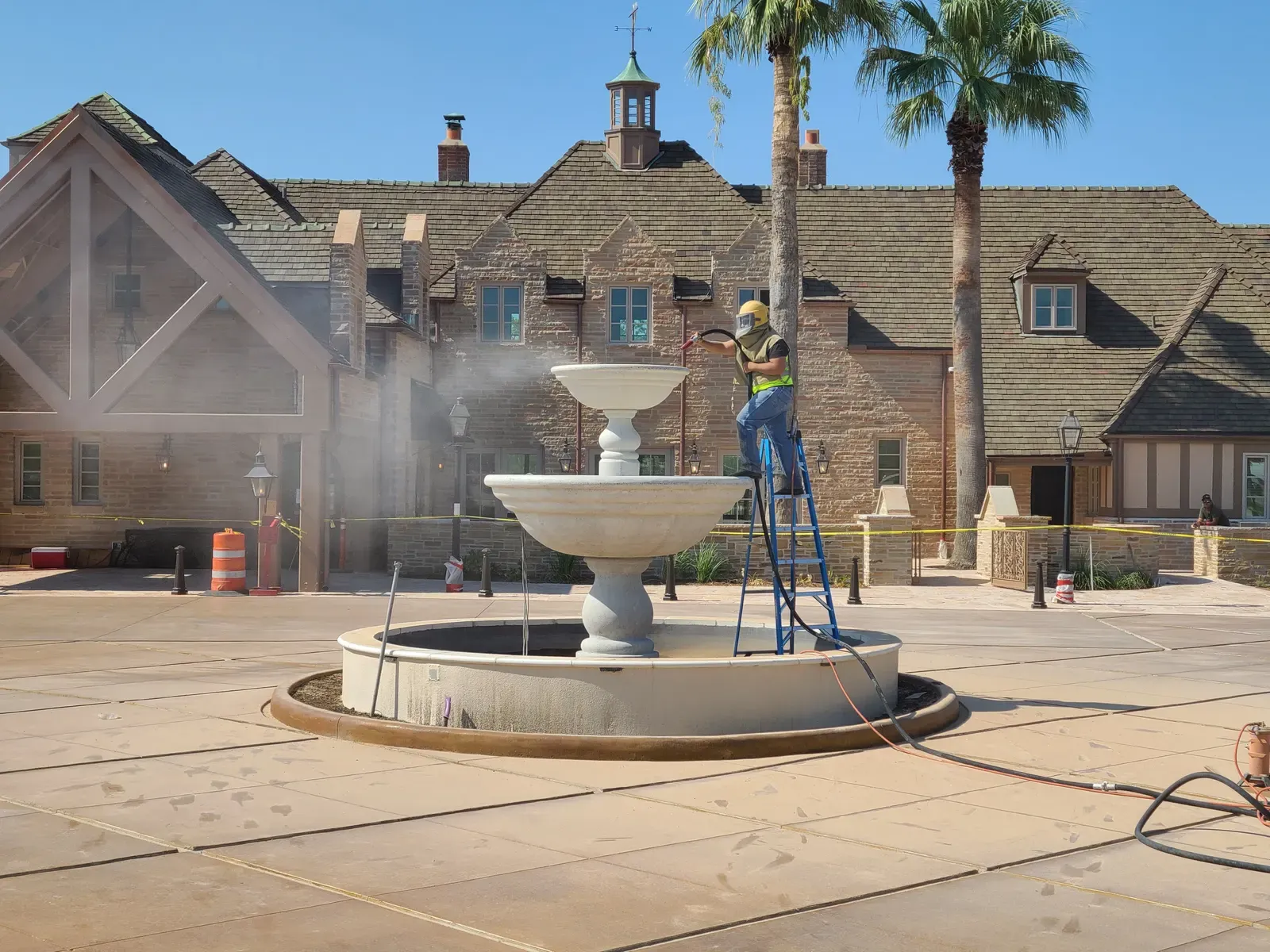 Worker on a ladder sandblasting a tiered courtyard fountain