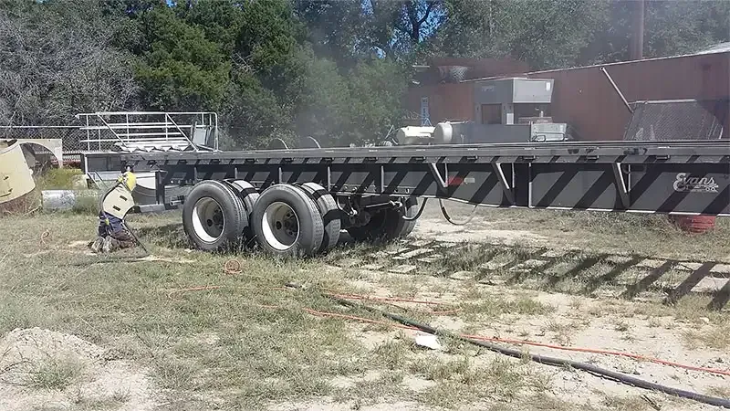 Crew member sandblasting a flatbed trailer chassis
