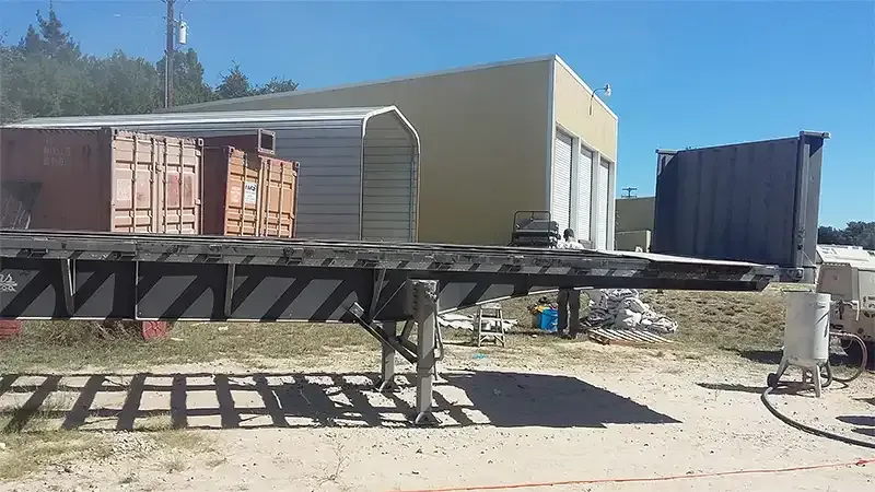 Flatbed trailer frame staged in a yard for steel sandblasting