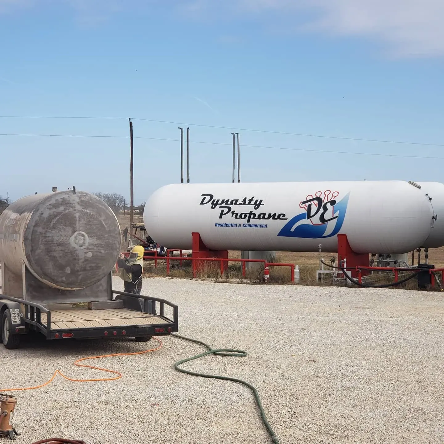 Industrial sandblasting rig beside a large propane storage tank