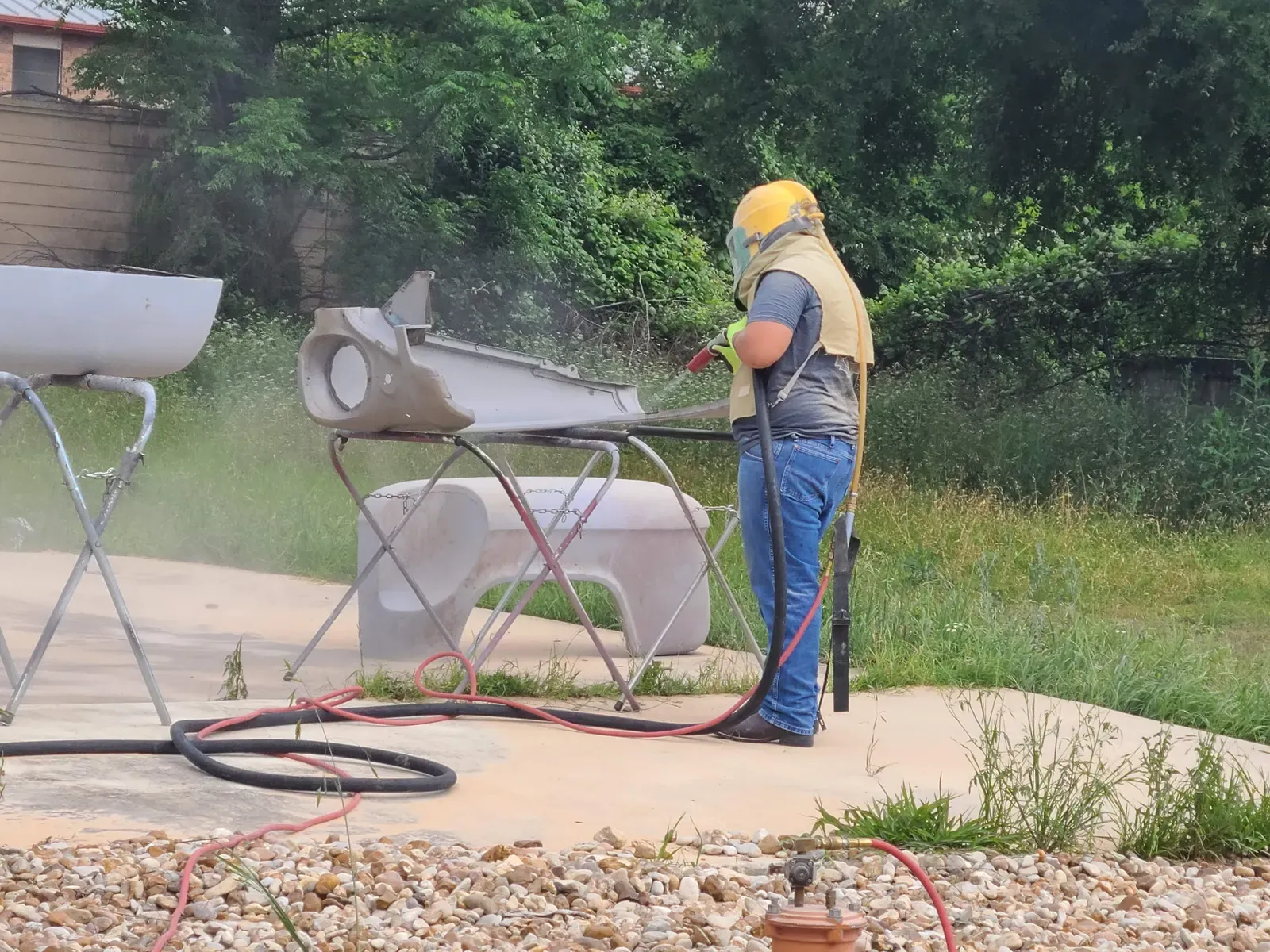 Blaster stripping paint from steel parts on stands outdoors