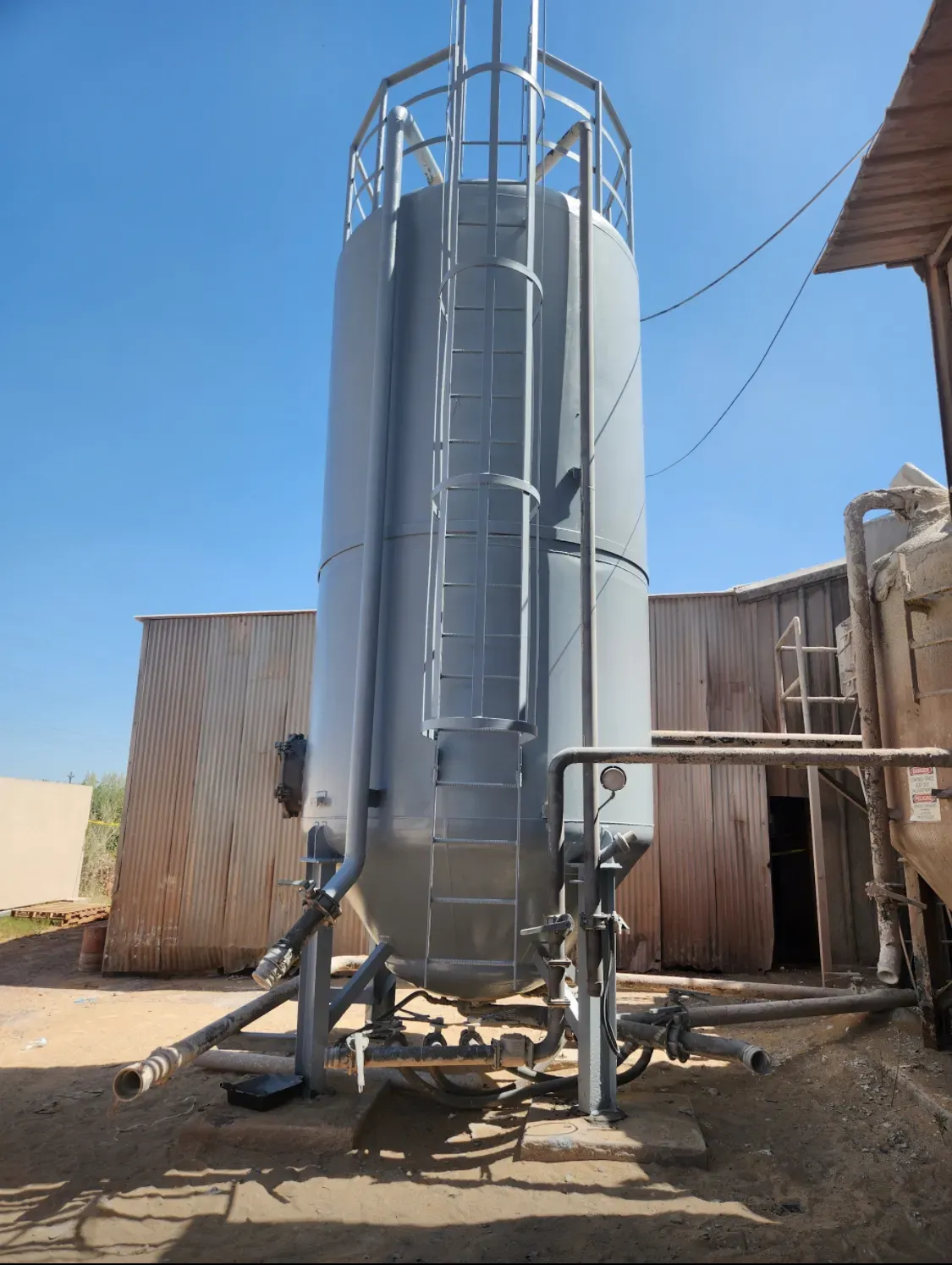 Tall steel storage silo with ladder cage awaiting surface prep