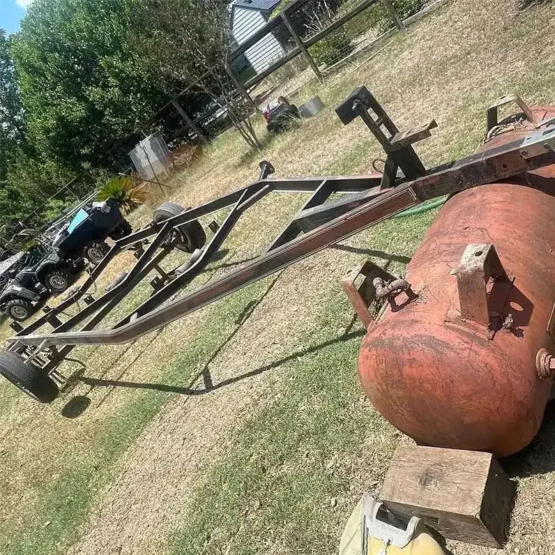 Sandblasted steel trailer frame and red air tank staged on grass for painting