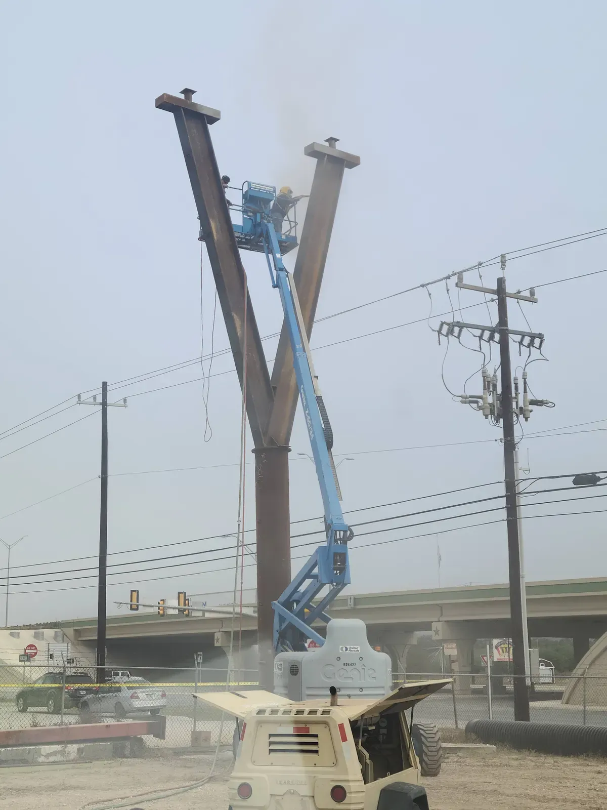 Steel Y-frame pole being blasted from a boom lift near power lines