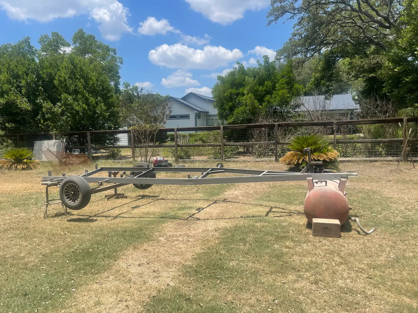 Bare steel trailer frame and tank sandblasted in a backyard