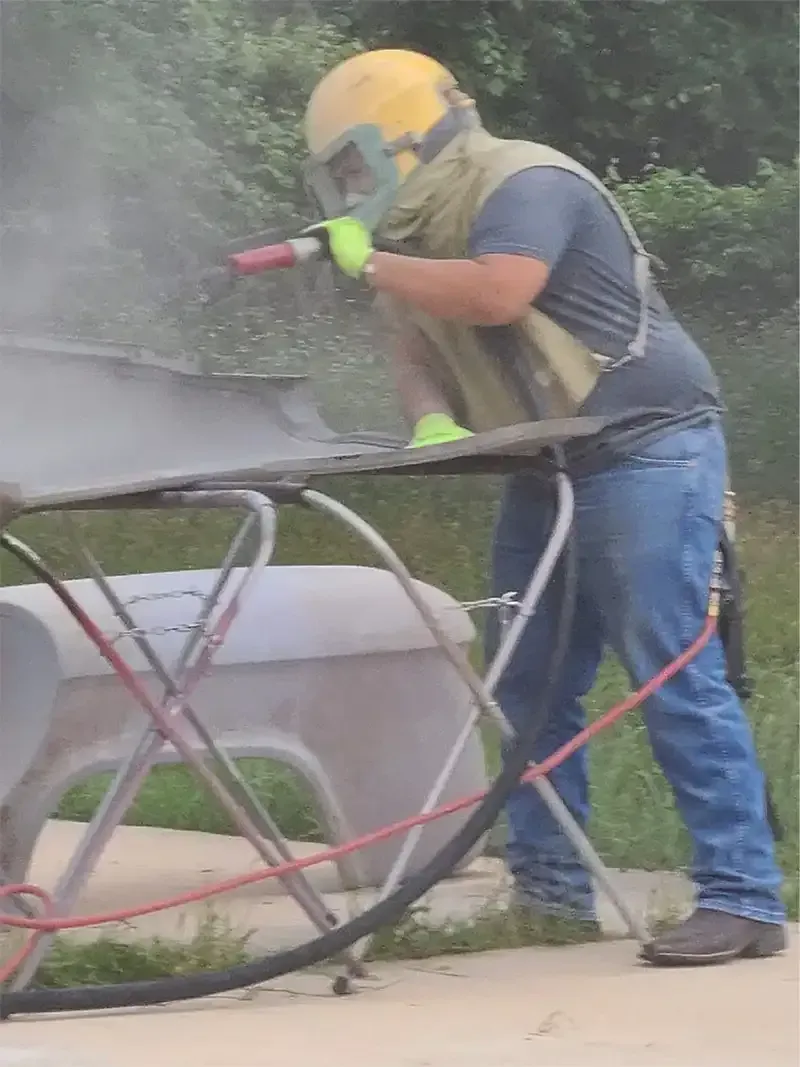 Blaster in a hood and respirator stripping paint from a vehicle panel