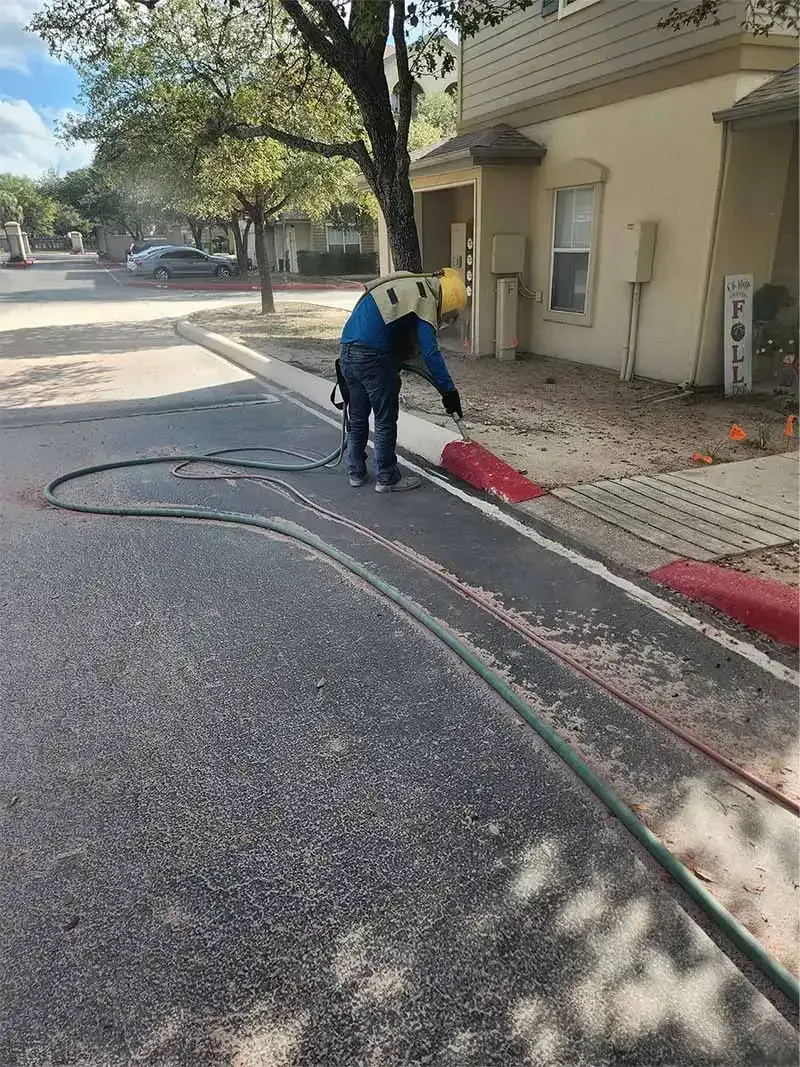 Technician blasting red curb paint along an apartment complex drive