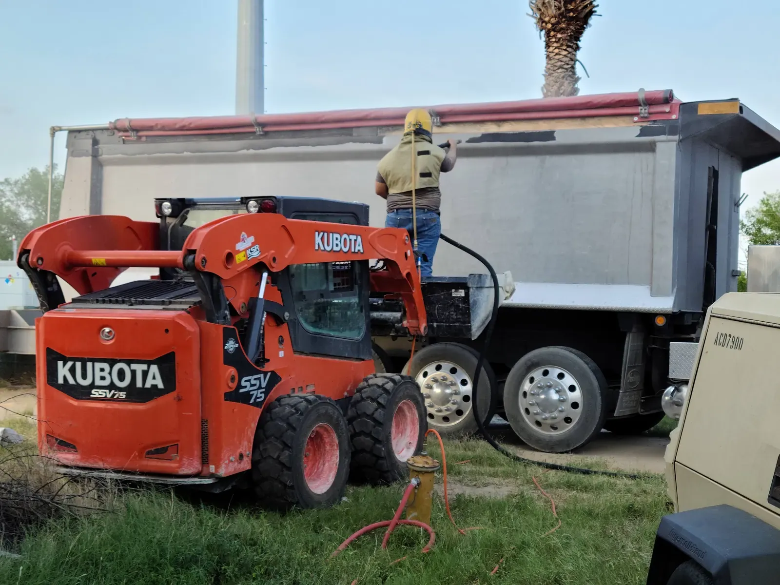 Dump truck box being sandblasted with a Kubota skid steer nearby