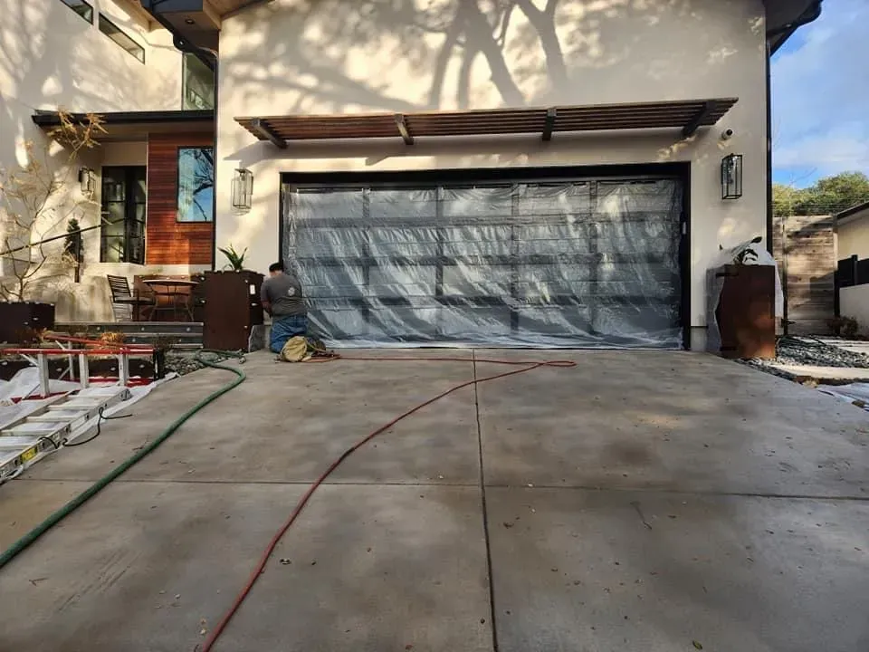 Garage door masked in plastic while a home’s concrete driveway is blasted
