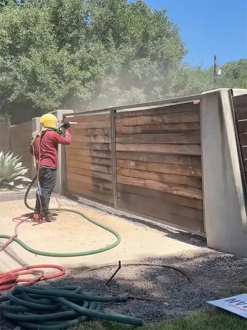 Technician sandblasting a horizontal cedar privacy fence