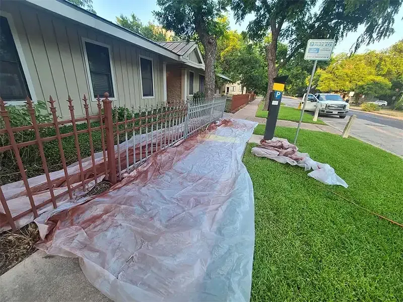 Iron fence line masked with plastic sheeting during sandblasting