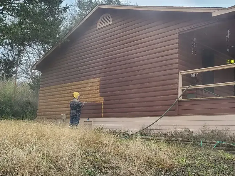 Technician sandblasting dark stain off log cabin siding