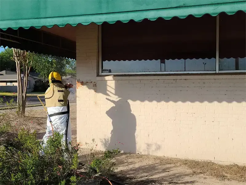 Blaster in a protective suit cleaning a painted brick building wall