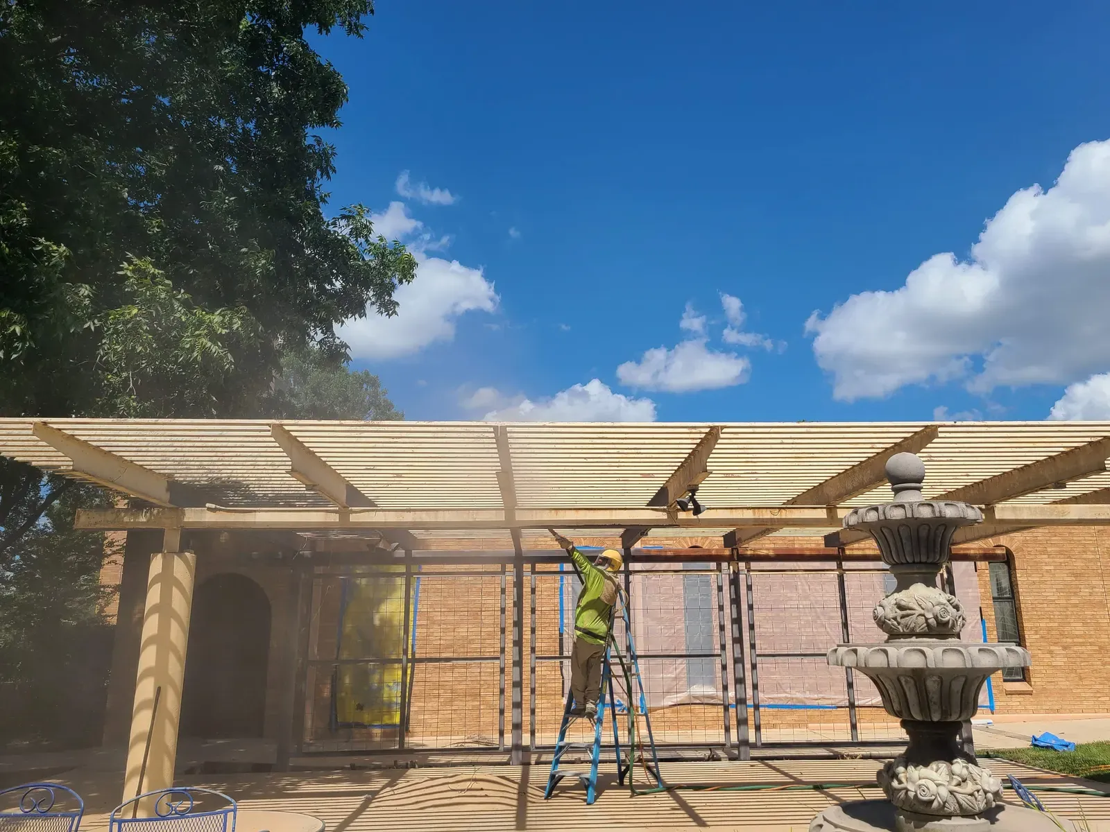 Technician sandblasting a wood pergola beside a brick home