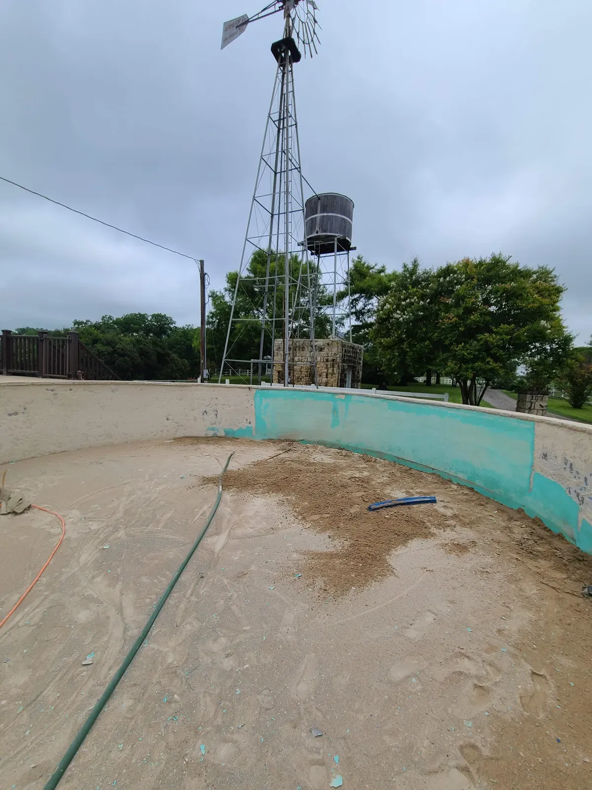 Empty swimming pool shell being sandblasted near a windmill