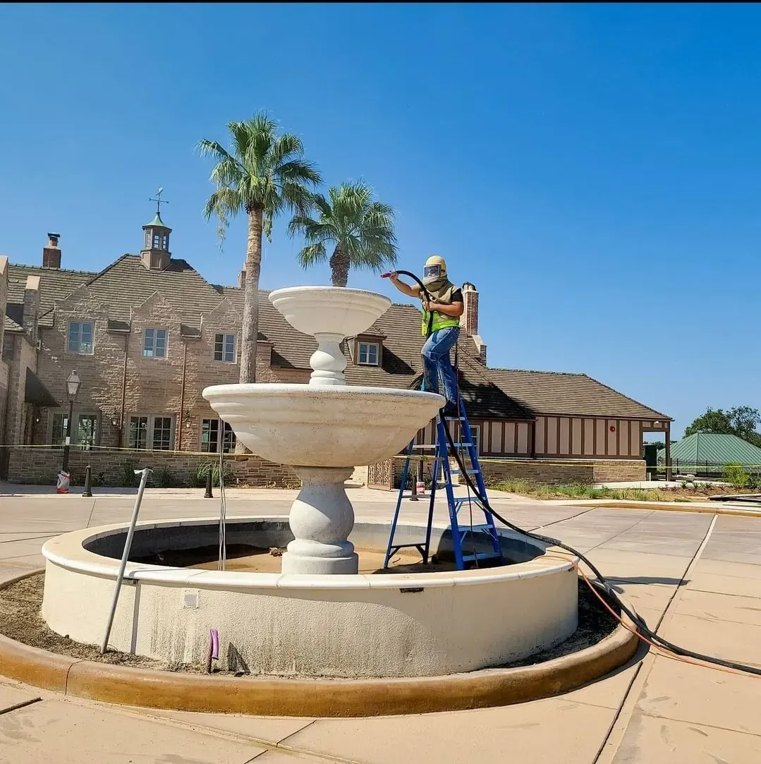 Technician on a ladder blasting a tiered stone courtyard fountain