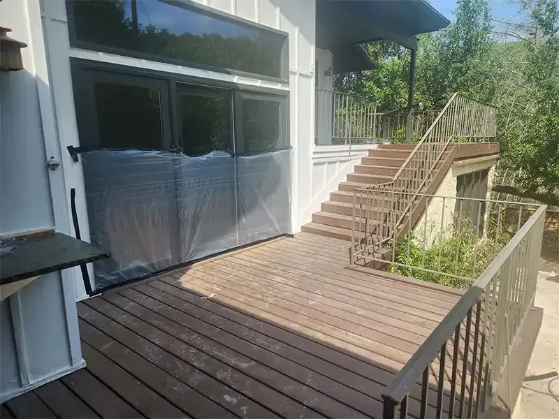 Weathered wood deck with windows masked in plastic before sandblasting